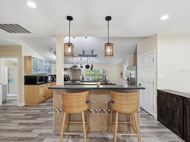 kitchen with stainless steel appliances, hanging light fixtures, vaulted ceiling, light hardwood / wood-style flooring, and a kitchen breakfast bar