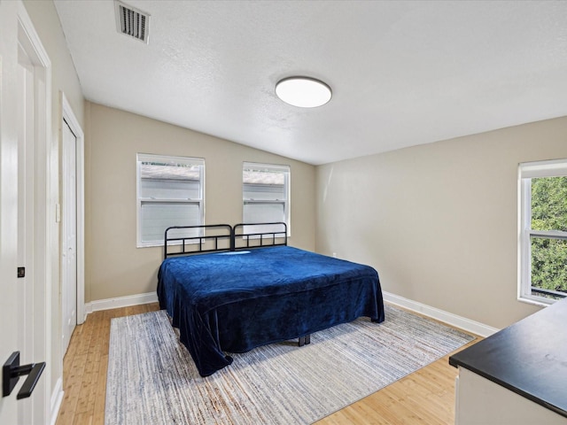 bedroom with vaulted ceiling, hardwood / wood-style floors, and a textured ceiling