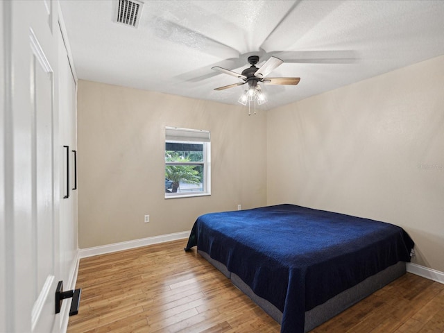 bedroom with ceiling fan, hardwood / wood-style flooring, and a textured ceiling