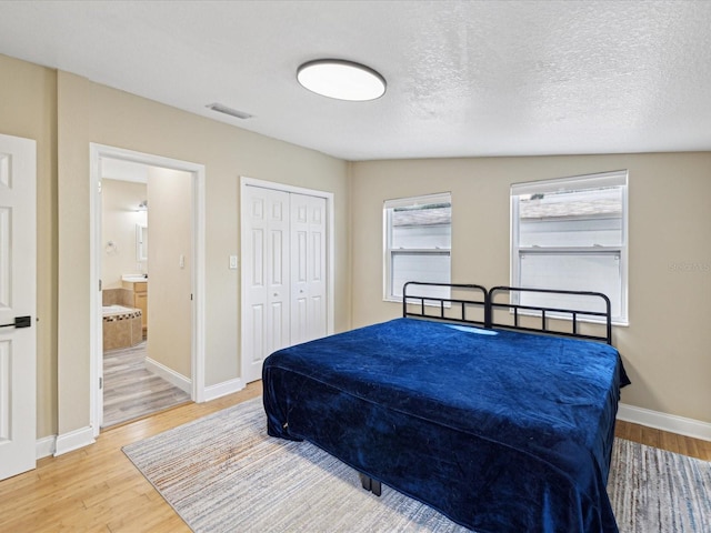 bedroom featuring wood-type flooring, a closet, vaulted ceiling, ensuite bath, and a textured ceiling