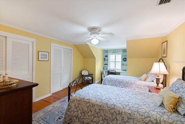 bedroom with multiple closets, crown molding, wood-type flooring, and ceiling fan