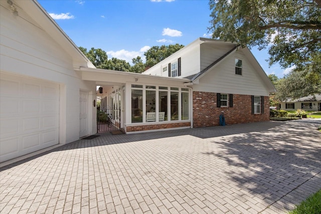 rear view of property featuring a garage, brick siding, and a sunroom