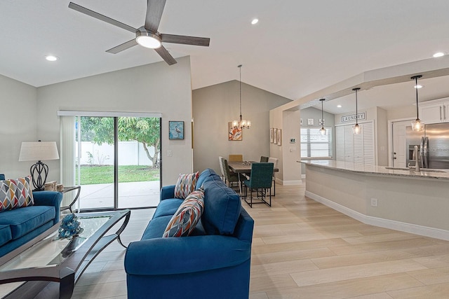 living room featuring lofted ceiling, light wood-style flooring, ceiling fan with notable chandelier, and baseboards