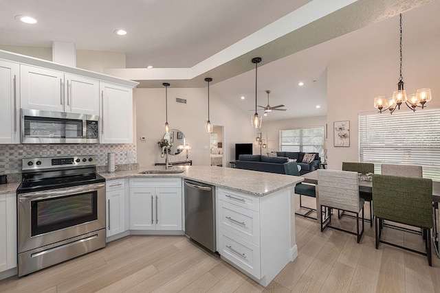 kitchen featuring light wood finished floors, a peninsula, stainless steel appliances, vaulted ceiling, and white cabinets