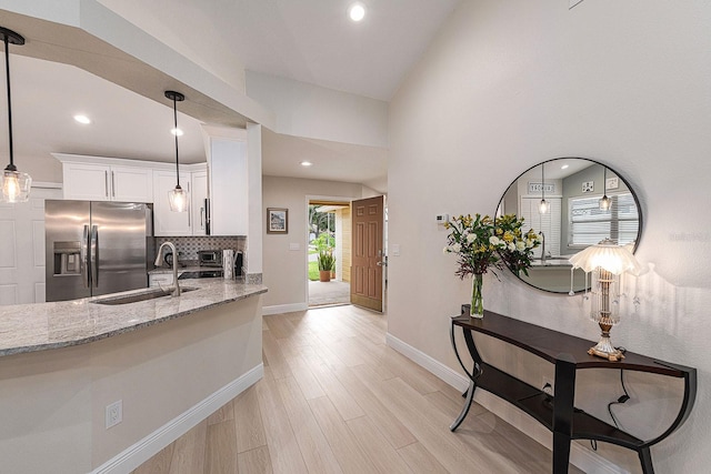 kitchen featuring light stone counters, a sink, stainless steel fridge, white cabinets, and light wood-type flooring