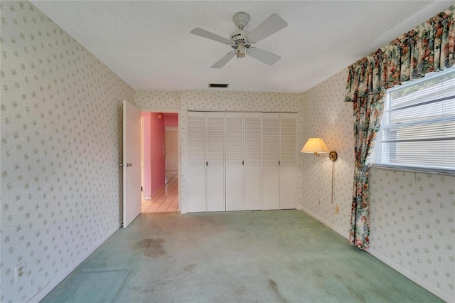 unfurnished bedroom with a textured ceiling, ceiling fan, a closet, and carpet floors