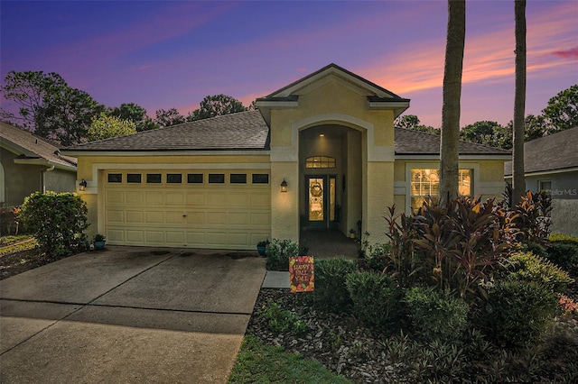 view of front facade featuring concrete driveway, roof with shingles, an attached garage, and stucco siding