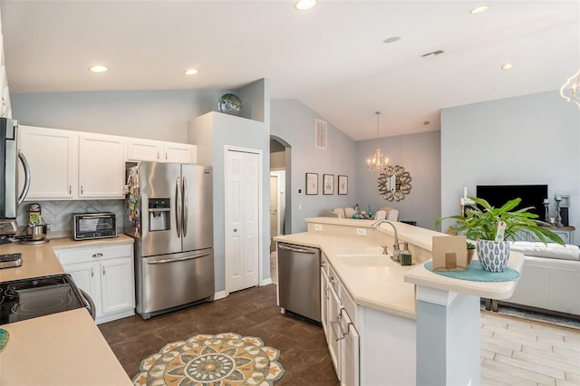 kitchen featuring arched walkways, stainless steel appliances, a sink, vaulted ceiling, and light countertops