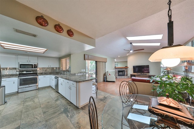 kitchen featuring appliances with stainless steel finishes, white cabinetry, vaulted ceiling with skylight, kitchen peninsula, and ceiling fan