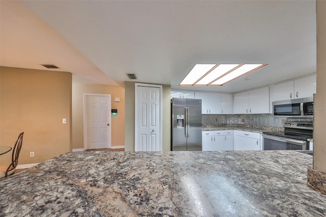 kitchen with white cabinetry, backsplash, stainless steel appliances, and stone counters