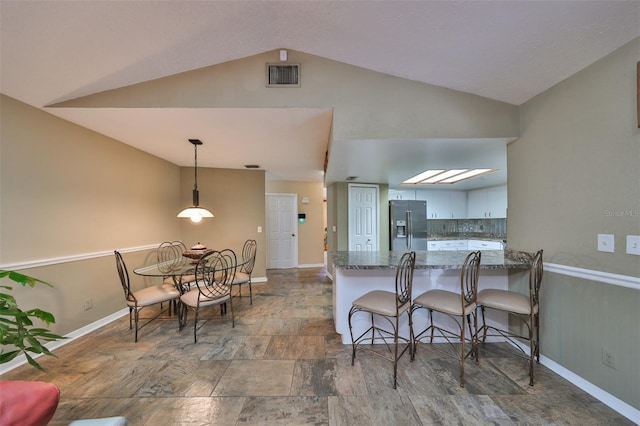 kitchen with dark stone countertops, vaulted ceiling, kitchen peninsula, a kitchen breakfast bar, and stainless steel fridge with ice dispenser