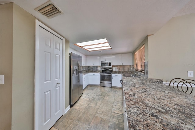 kitchen featuring a skylight, sink, decorative backsplash, appliances with stainless steel finishes, and white cabinets