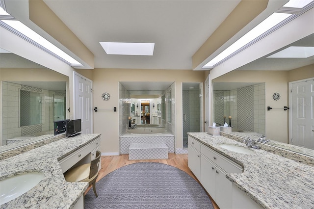 bathroom featuring a skylight, hardwood / wood-style flooring, shower with separate bathtub, and vanity