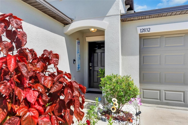 entrance to property with a garage and stucco siding