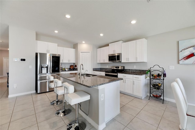 kitchen with white cabinets, appliances with stainless steel finishes, sink, dark stone counters, and a kitchen island with sink