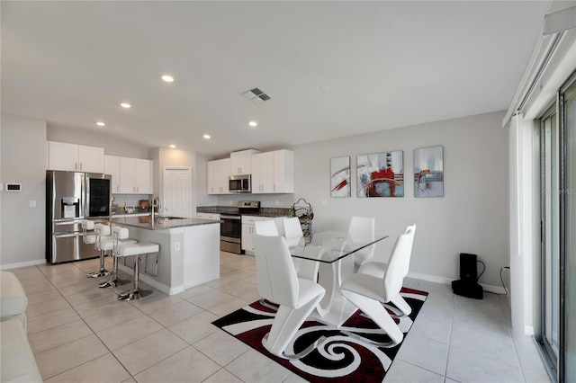 kitchen featuring vaulted ceiling, stainless steel appliances, white cabinetry, an island with sink, and a breakfast bar area