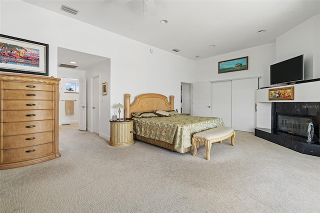 bedroom featuring a closet, ceiling fan, light colored carpet, and a premium fireplace