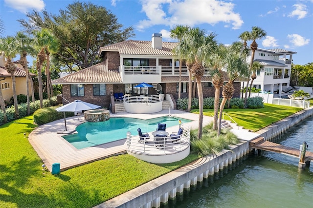 rear view of property with a balcony, a water view, a patio area, a yard, and a pool with hot tub