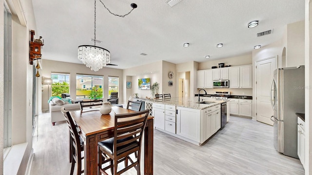 kitchen featuring white cabinetry, hanging light fixtures, a center island with sink, appliances with stainless steel finishes, and light stone countertops