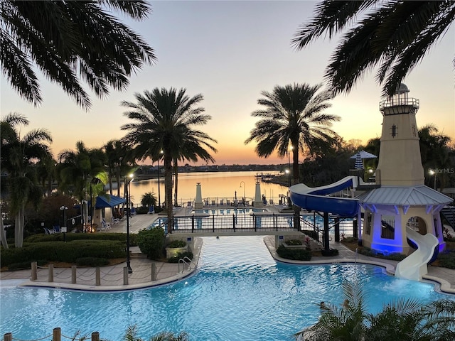 pool at dusk featuring a water view, a water slide, and a patio area