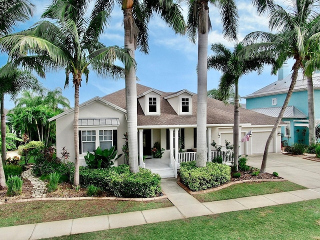 view of front facade featuring a porch, an attached garage, concrete driveway, stucco siding, and roof with shingles