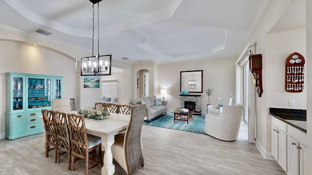 dining area with a raised ceiling, light wood finished floors, a chandelier, a stone fireplace, and baseboards