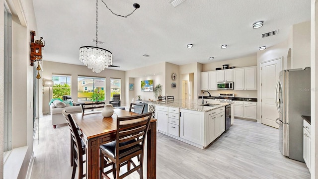 kitchen featuring stainless steel appliances, a chandelier, light wood-type flooring, a sink, and a textured ceiling