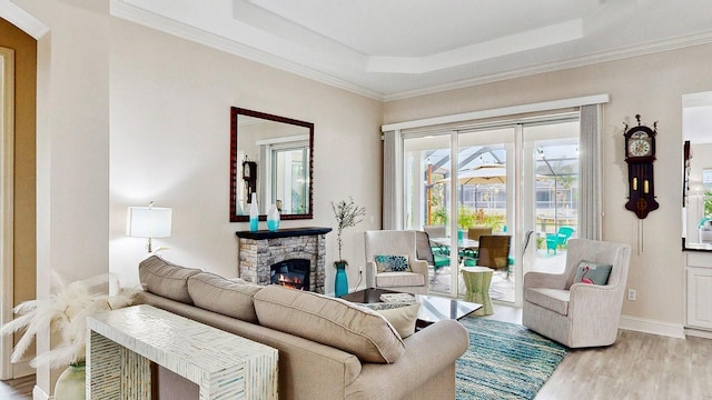living area with a tray ceiling, wood finished floors, a stone fireplace, crown molding, and baseboards