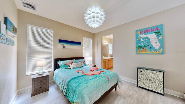 bedroom featuring baseboards, light wood finished floors, and ensuite bath