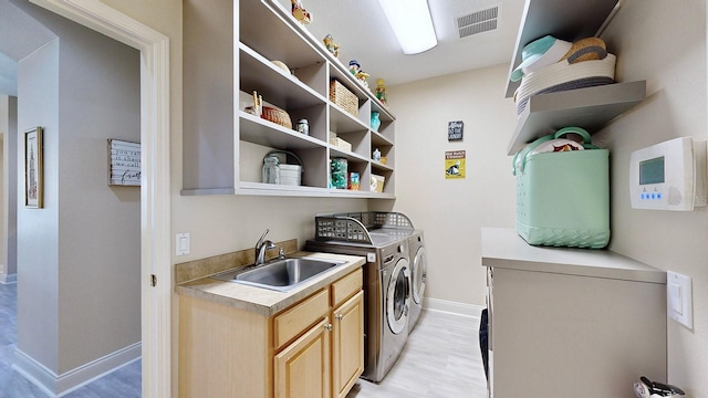 clothes washing area with washing machine and dryer, baseboards, cabinet space, and light wood-style flooring