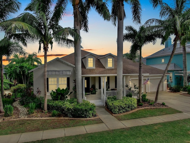 view of front facade featuring covered porch, an attached garage, driveway, stucco siding, and a shingled roof