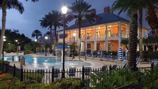pool at twilight with fence, a patio area, and a community pool