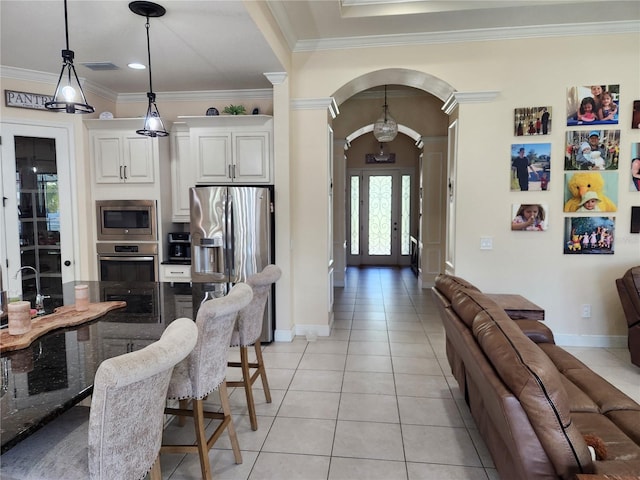 kitchen featuring pendant lighting, ornamental molding, stainless steel appliances, a breakfast bar, and white cabinets