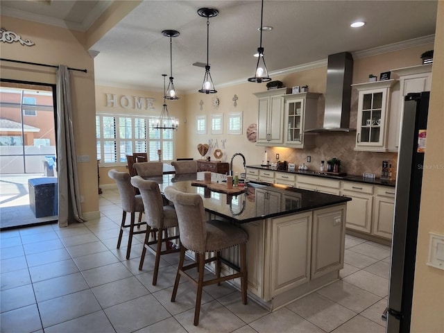 kitchen featuring crown molding, stainless steel fridge, wall chimney exhaust hood, a breakfast bar area, and a kitchen island with sink