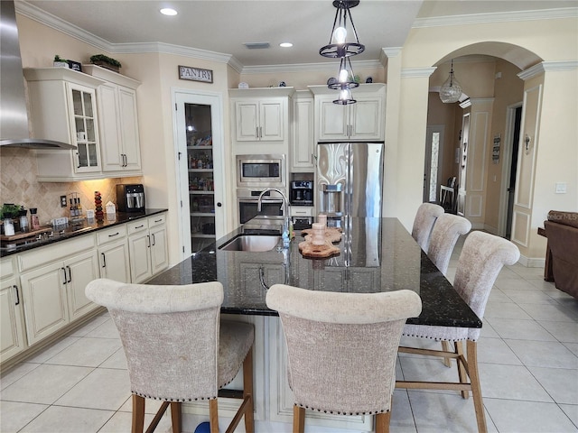 kitchen featuring wall chimney range hood, stainless steel appliances, a center island with sink, and sink