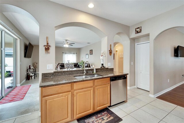 kitchen featuring dark stone countertops, light tile patterned floors, sink, ceiling fan, and stainless steel dishwasher