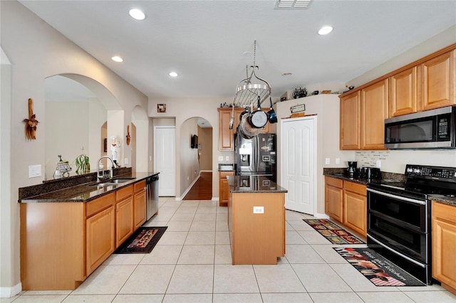 kitchen featuring dark stone countertops, light tile patterned floors, stainless steel appliances, a kitchen island, and sink