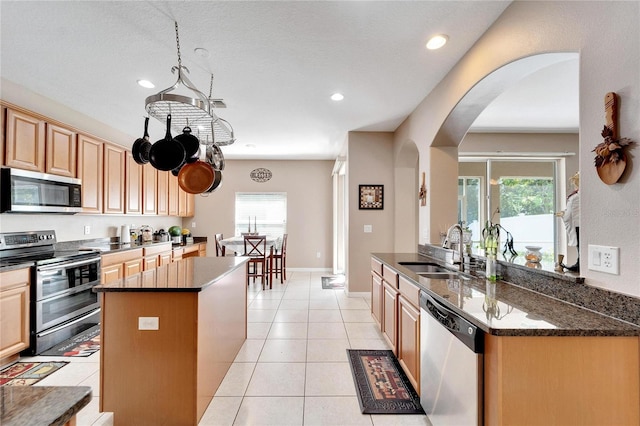 kitchen with light tile patterned floors, a center island, stainless steel appliances, sink, and dark stone counters