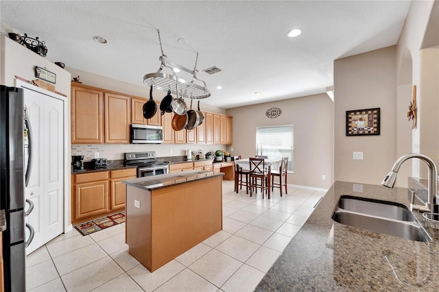 kitchen with a textured ceiling, a center island, sink, appliances with stainless steel finishes, and light tile patterned flooring