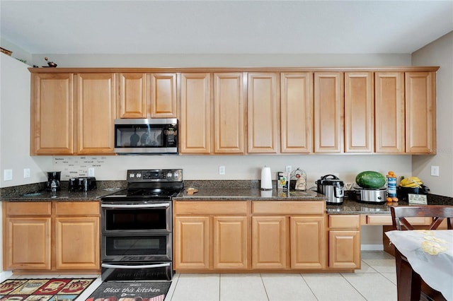 kitchen with stainless steel appliances, dark stone countertops, and light tile patterned flooring