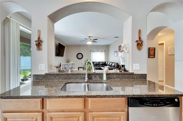 kitchen featuring dark stone countertops, light brown cabinets, stainless steel dishwasher, and ceiling fan