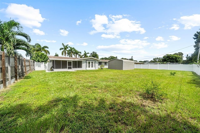 view of yard with a shed, an outdoor structure, a fenced backyard, and a sunroom