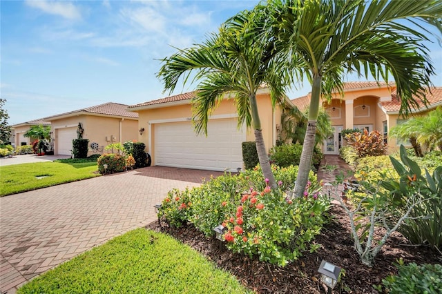 mediterranean / spanish house featuring decorative driveway, a tiled roof, an attached garage, and stucco siding