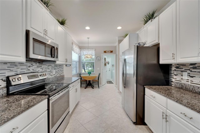 kitchen featuring dark stone countertops, an inviting chandelier, stainless steel appliances, white cabinetry, and ornamental molding