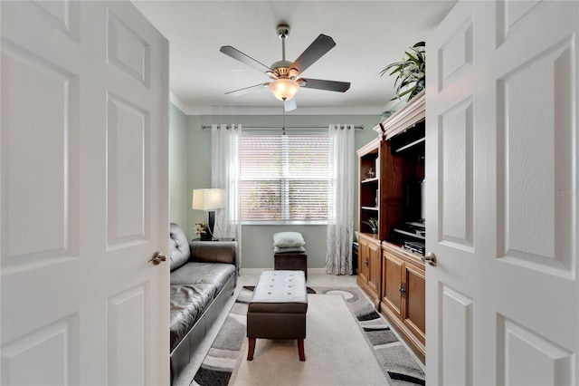 sitting room featuring ceiling fan, baseboards, and crown molding