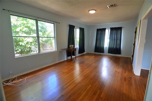 spare room featuring a textured ceiling, baseboards, visible vents, and hardwood / wood-style flooring