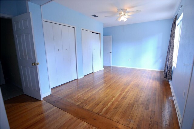 unfurnished bedroom with two closets, ceiling fan, visible vents, wood-type flooring, and baseboards