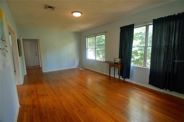 empty room featuring visible vents, hardwood / wood-style flooring, baseboards, and a textured ceiling