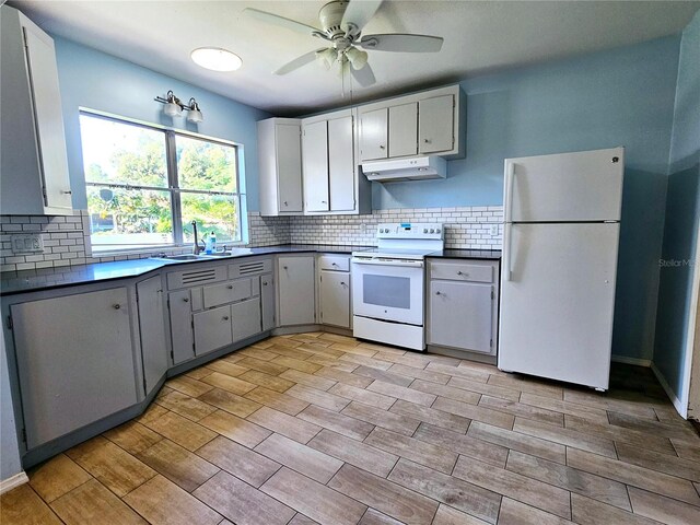kitchen with white appliances, a ceiling fan, dark countertops, under cabinet range hood, and a sink