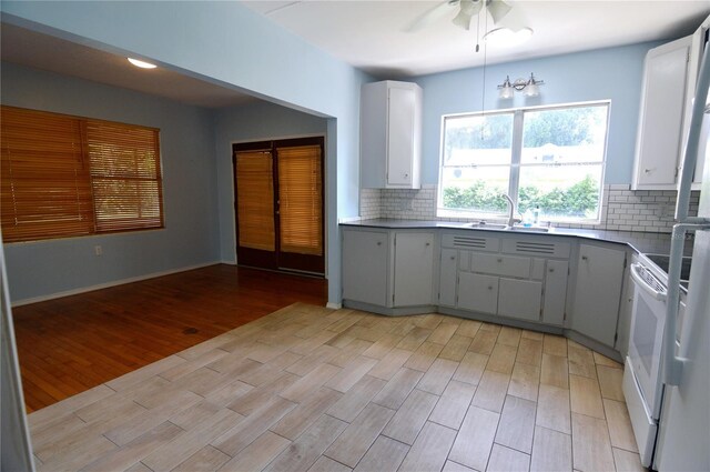 kitchen featuring light wood-style floors, a sink, white range with electric cooktop, and decorative backsplash